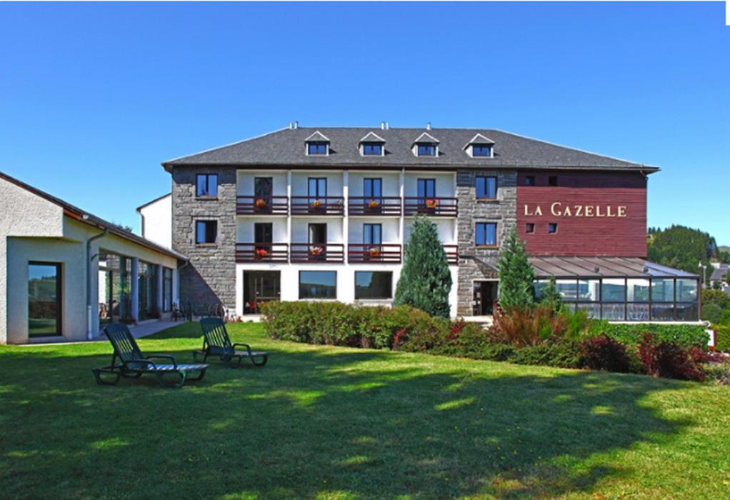 un grand bâtiment avec deux bancs dans l'herbe dans l'établissement Hotel La Gazelle, à Besse-et-Saint-Anastaise