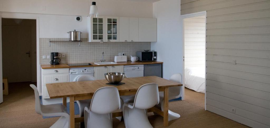 a kitchen with a wooden table and white chairs at Le Château de Sable in Plougasnou