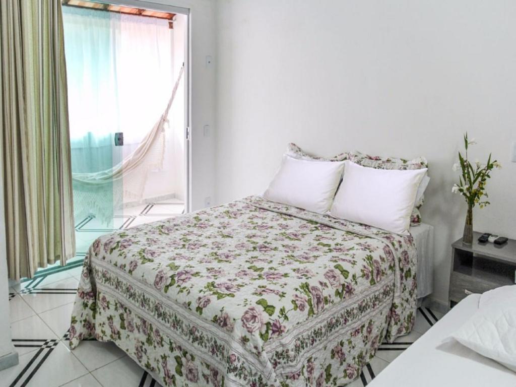 a bedroom with a bed with a floral bedspread and a window at Restaurante & Pousada Almescla in Santa Cruz Cabrália