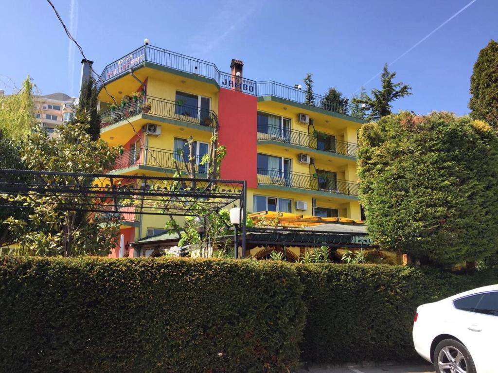 um edifício amarelo e vermelho com um carro estacionado na frente em Hotel Jambo em Golden Sands