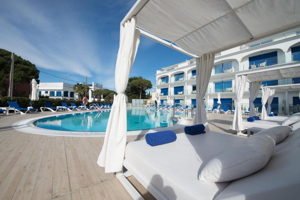 a swimming pool with chairs and a white umbrella at Masd Mediterraneo Hotel Apartamentos Spa in Castelldefels