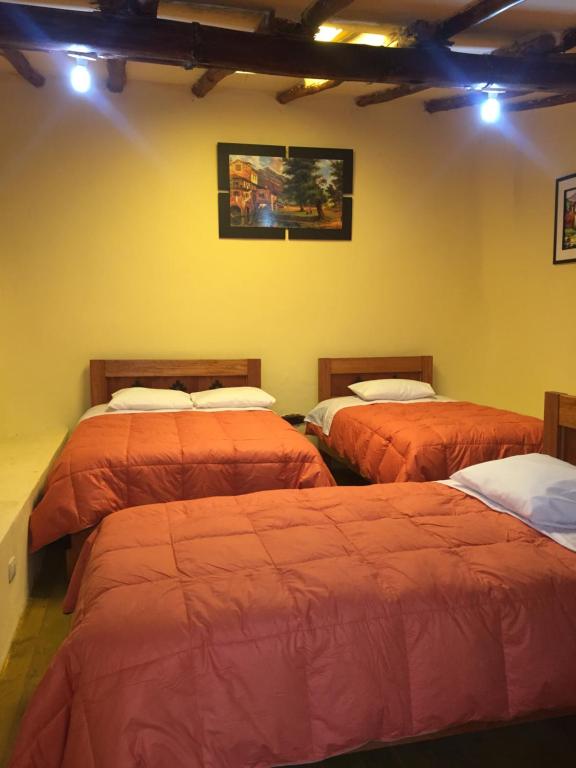 3 camas en una habitación con paredes amarillas en Rumi Sonqo Hostel, en Ollantaytambo