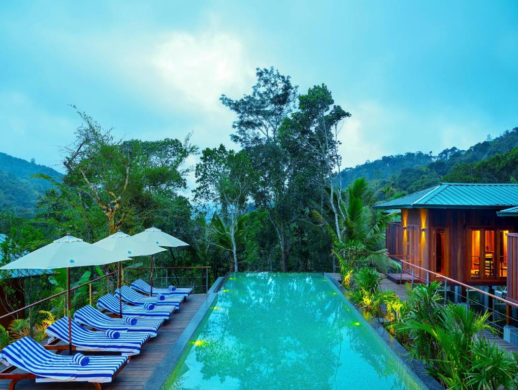 a pool with chairs and umbrellas next to a house at Niraamaya Retreats Cardamom Club in Thekkady