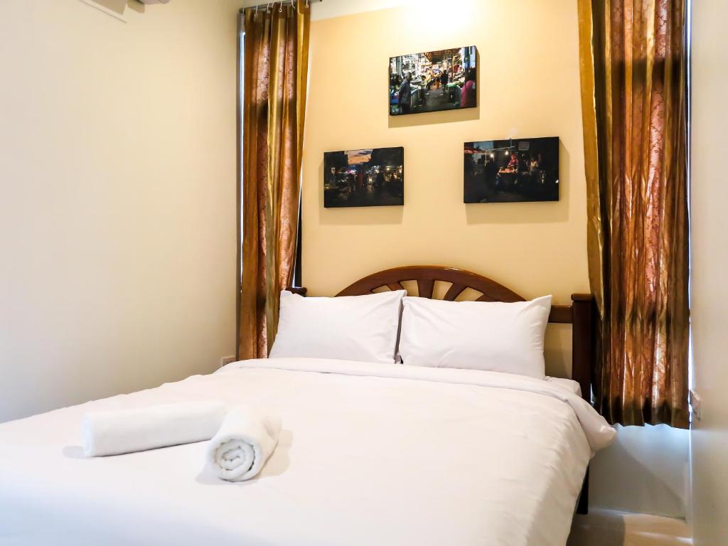 um quarto com uma cama com lençóis brancos e fotografias na parede em โรงแรมนางรอง em Nang Rong