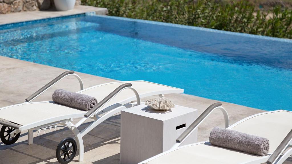 two chairs and a table next to a swimming pool at Mykonos Panormos Villas in Mykonos