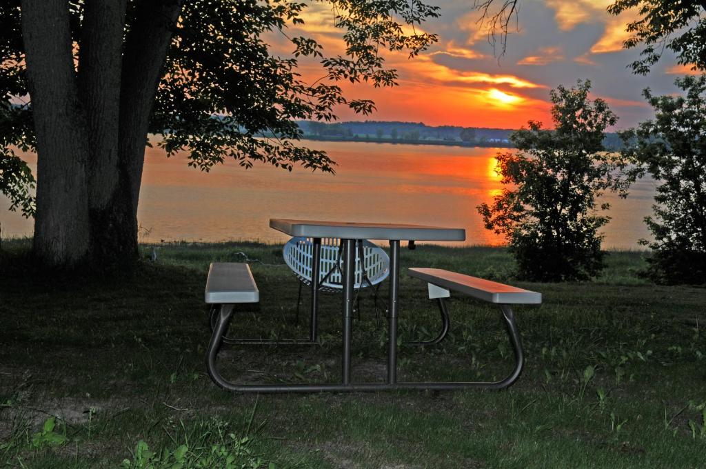 a picnic table with two benches in front of a lake at Motel Le Charentais in Sorel