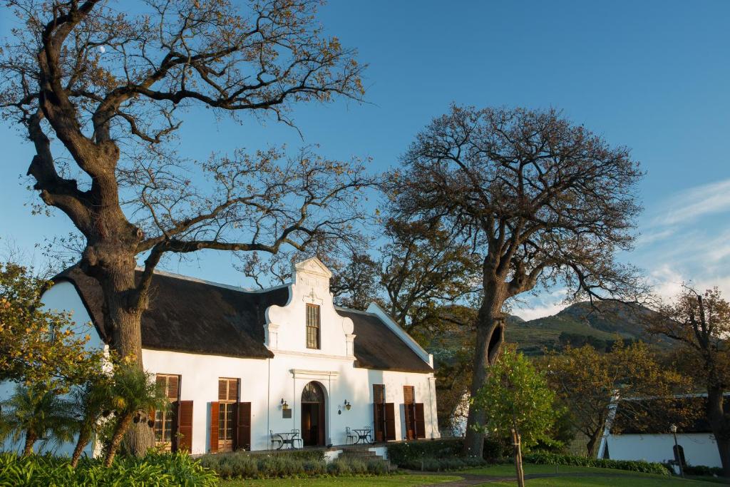 ein weißes Haus mit Bäumen im Vordergrund in der Unterkunft Laborie Estate in Paarl