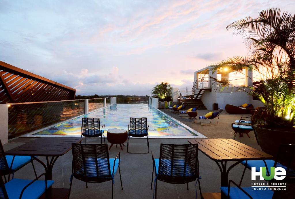 a balcony with tables and chairs and a swimming pool at Hue Hotels and Resorts Puerto Princesa Managed by HII in Puerto Princesa City