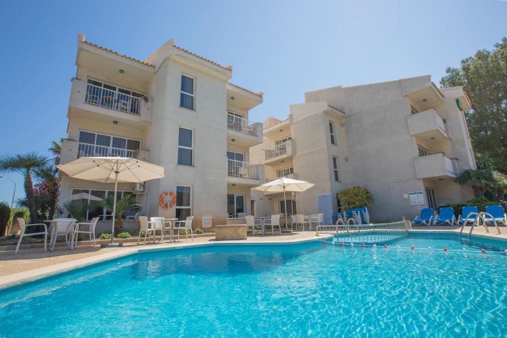 a pool with chairs and umbrellas in front of a building at Apartamentos Massol in Port de Pollensa