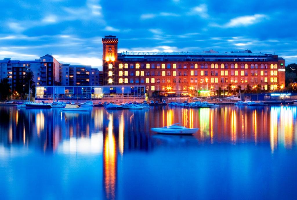 un grand bâtiment avec des bateaux dans l'eau la nuit dans l'établissement Holiday Club Tampereen Kehräämö, à Tampere