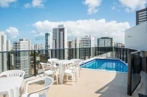 uma varanda com mesas e cadeiras brancas e uma piscina em Jaqueira Home Service no Recife
