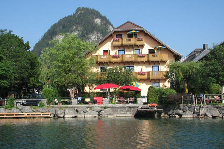 a building with tables and umbrellas next to a lake at Haus am See in Fuschl am See