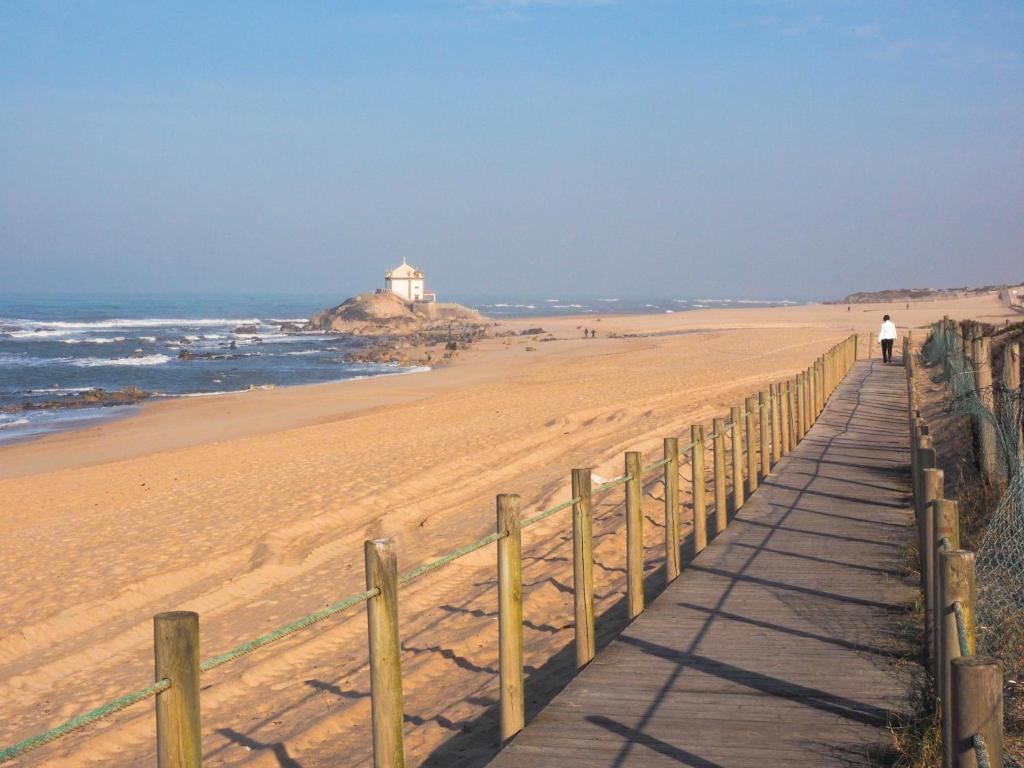a boardwalk on the beach with a lighthouse in the background at Oporto Beach House in Arcozelo