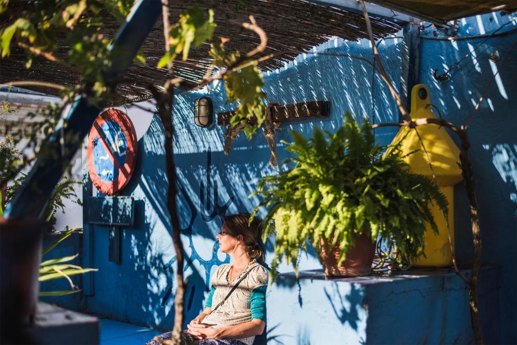 een vrouw die voor een blauwe muur met planten zit bij Casa Caracol in Cádiz