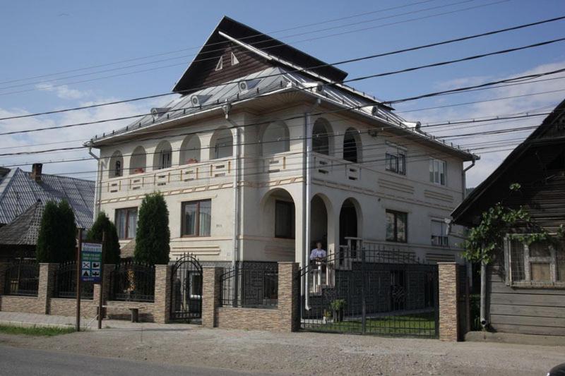 Une grande maison blanche avec un homme sur le balcon dans l'établissement Pension Bud, à Onceşti
