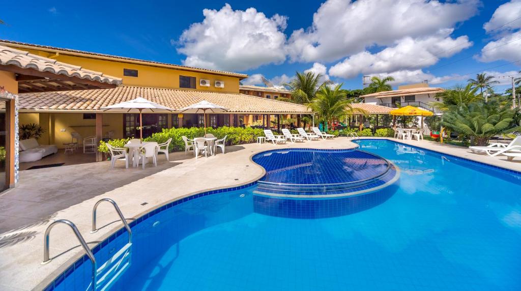 una piscina en un complejo con mesas y sillas en Porto Geraes Praia Hotel, en Porto Seguro
