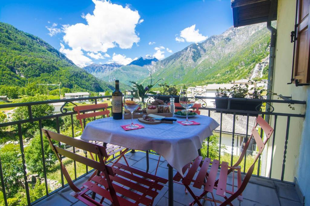 a table with wine glasses on a balcony with mountains at Ca' Nei Ronchi Bregaglia in Piuro