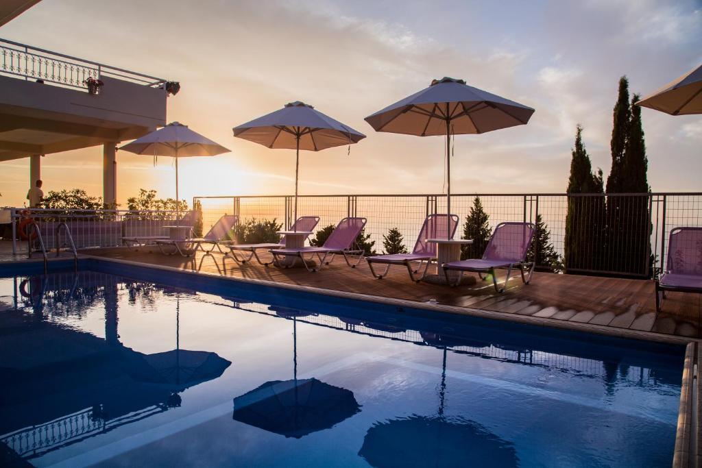 a swimming pool with purple chairs and umbrellas at Amalia Apartments in Exanthia