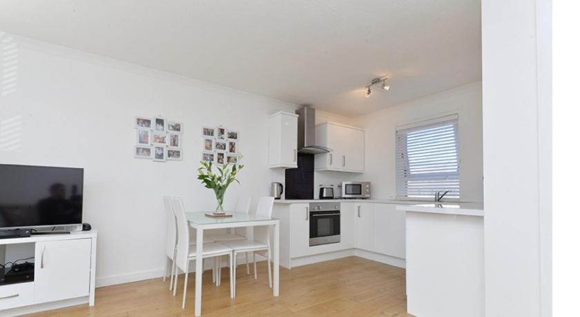 eine Küche mit weißen Schränken, einem Tisch und einem TV in der Unterkunft Edinburgh Seaside Apartment in Edinburgh