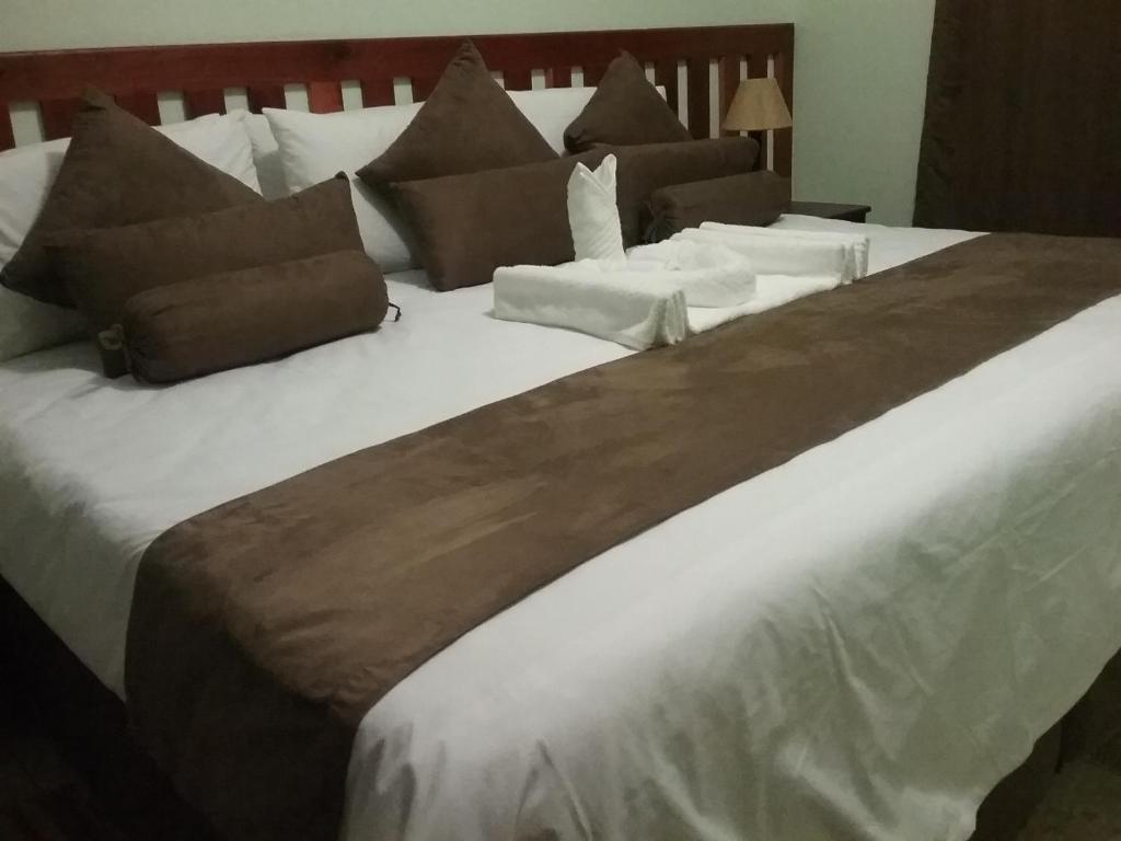 1 cama grande con sábanas blancas y almohadas marrones en Masikiro Self Catering, en Kasane