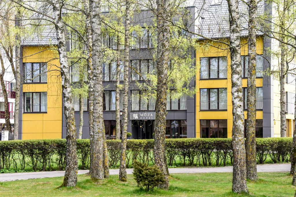 a yellow building with trees in front of it at Muza Hotel in Palanga