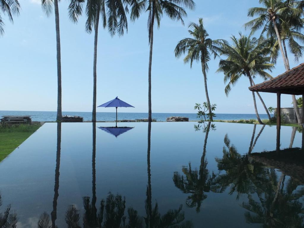 an infinity pool with palm trees and an umbrella at The Amrita - Salt Farm Villas in Tejakula