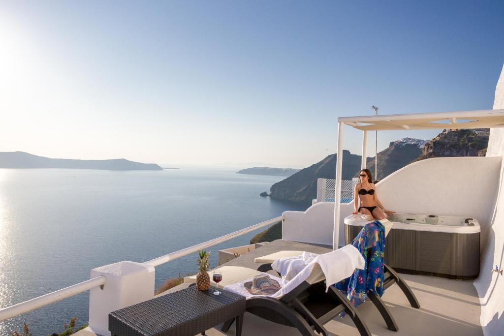 a woman sitting on the edge of a balcony overlooking the ocean at Asma Suites in Fira