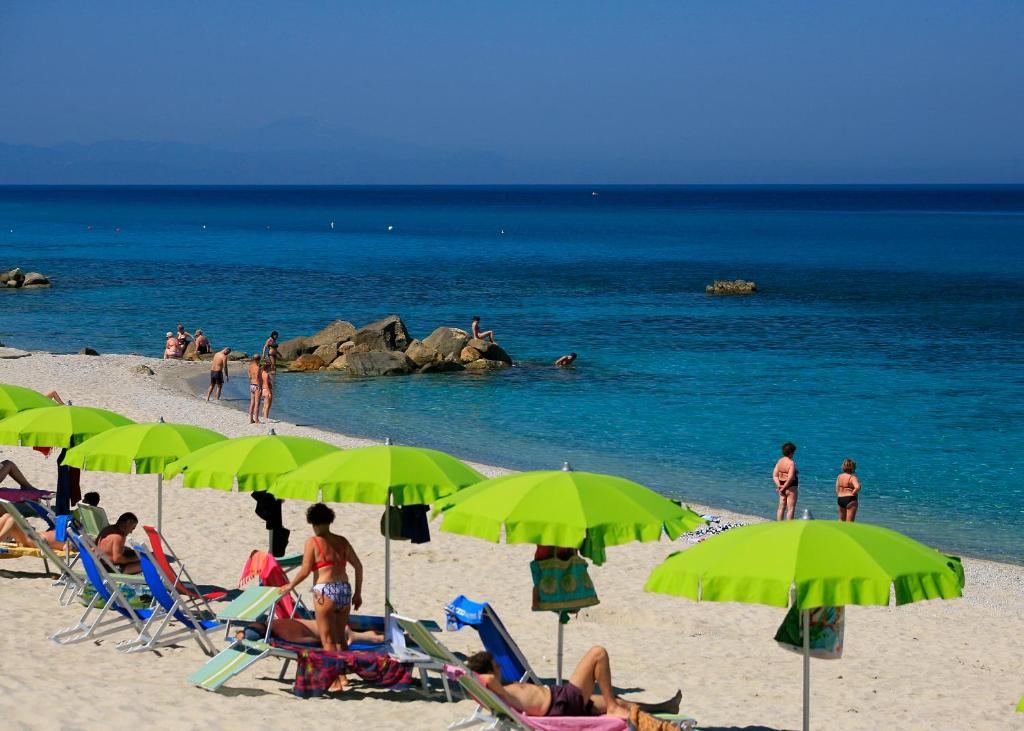 a group of people sitting on a beach with green umbrellas at Villaggio Athragon in Capo Vaticano