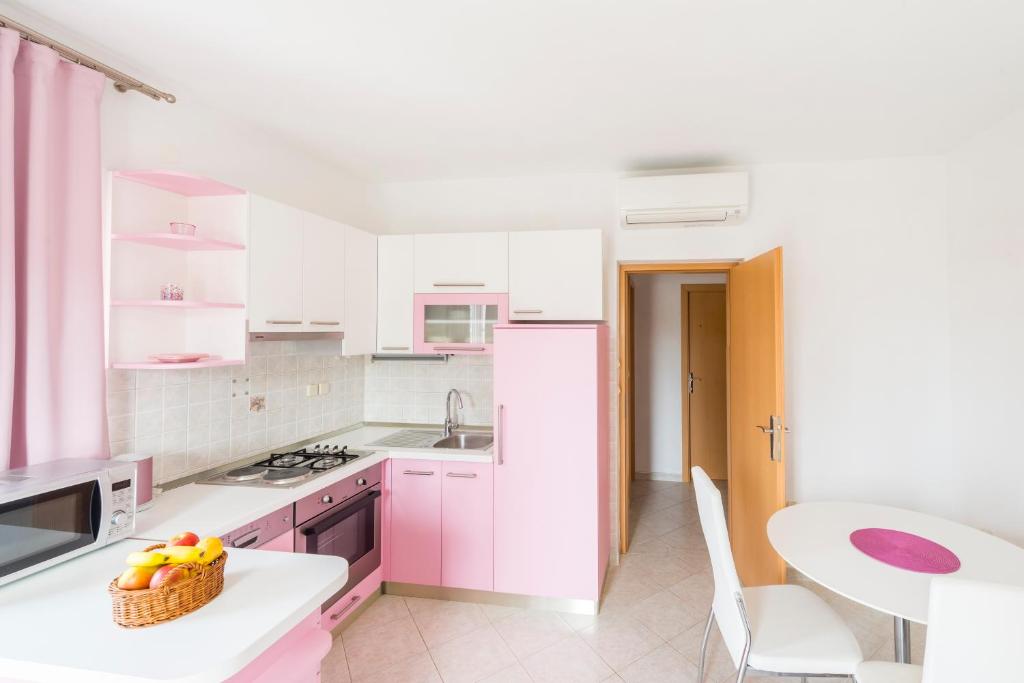 a white kitchen with pink cabinets and a table at Apartments Nikolina in Hvar