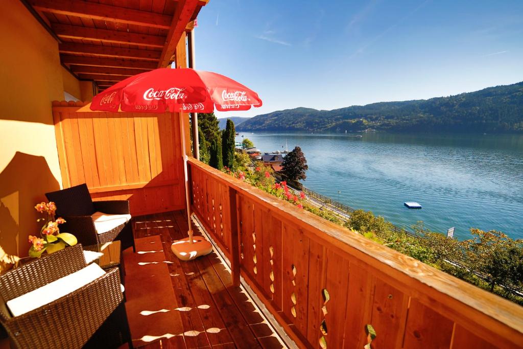 a balcony with a cocacola umbrella and a view of a lake at Pension Sedlak in Millstatt