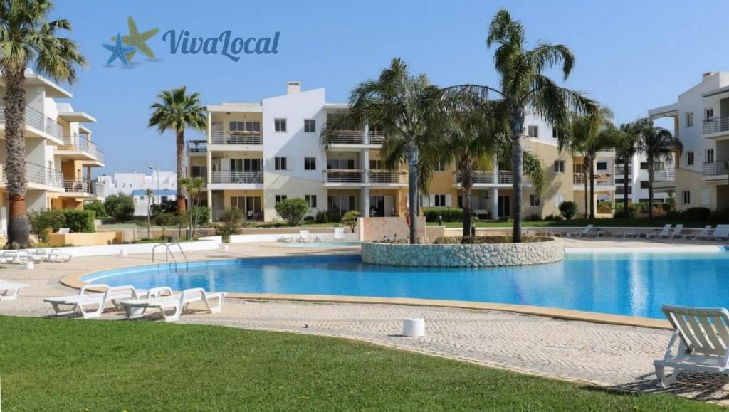 uma piscina num resort com palmeiras e edifícios em Vila da Praia - Apartamento Viva Local em Alvor