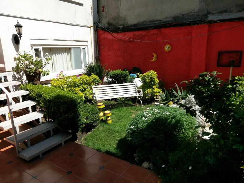 a garden with a bench next to a red wall at Anys Hostal in Mexico City