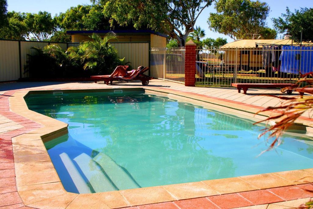 a swimming pool in a yard with a bench next to it at Coral Coast Tourist Park in Carnarvon