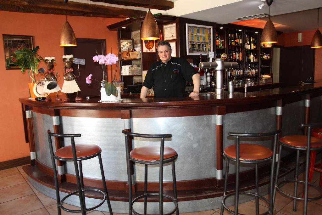 a man standing behind a bar with stools at Au Bon Accueil in Arvieu