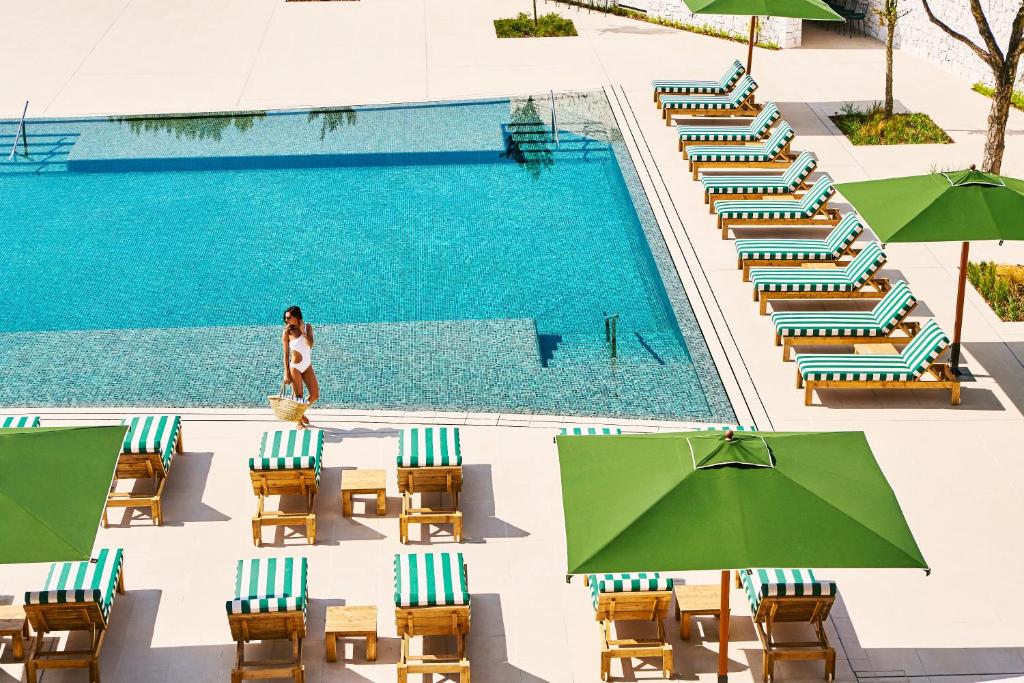 Eine Frau steht neben einem Pool mit Stühlen und Sonnenschirmen in der Unterkunft Camiral Golf & Wellness - Leading Hotel of the World in Caldes de Malavella