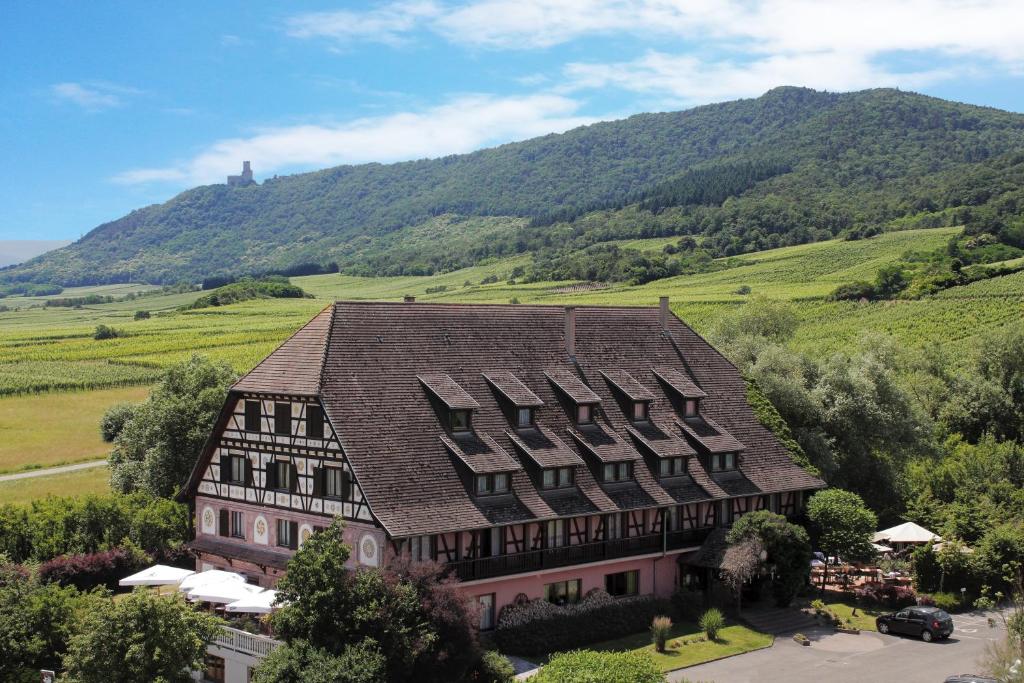 un grand bâtiment avec une montagne en arrière-plan dans l'établissement Hôtel Restaurant Verger des Châteaux, The Originals Relais, proche Sélestat, à Dieffenthal