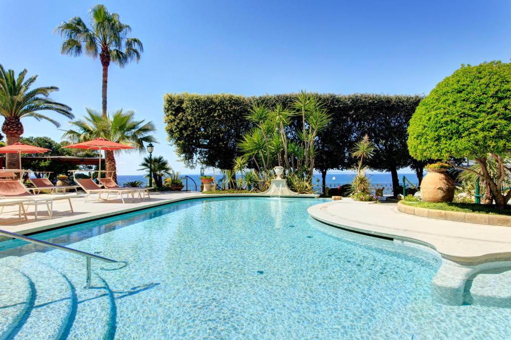 a swimming pool with chairs and palm trees and the ocean at Grand Hotel Ambasciatori in Sorrento