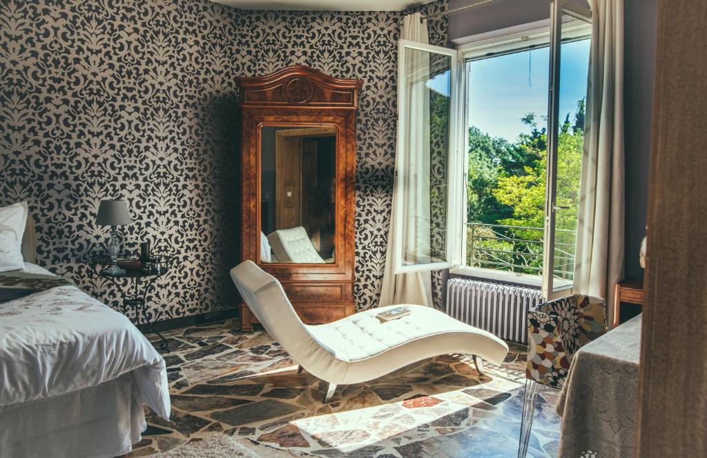 1 dormitorio con silla, espejo y ventana en Le Jardin de LaCoste, en Narbona