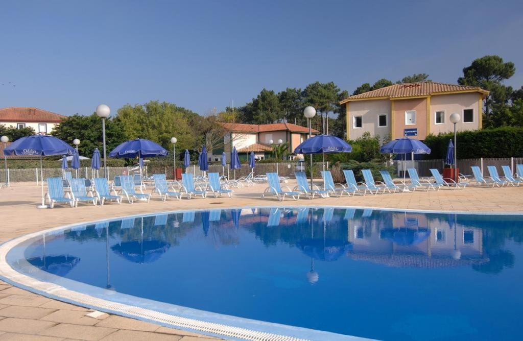 a swimming pool with chairs and blue umbrellas at Residence Sun Hols Villas du Lac - Appartement 2 piéces 4 pers in Soustons