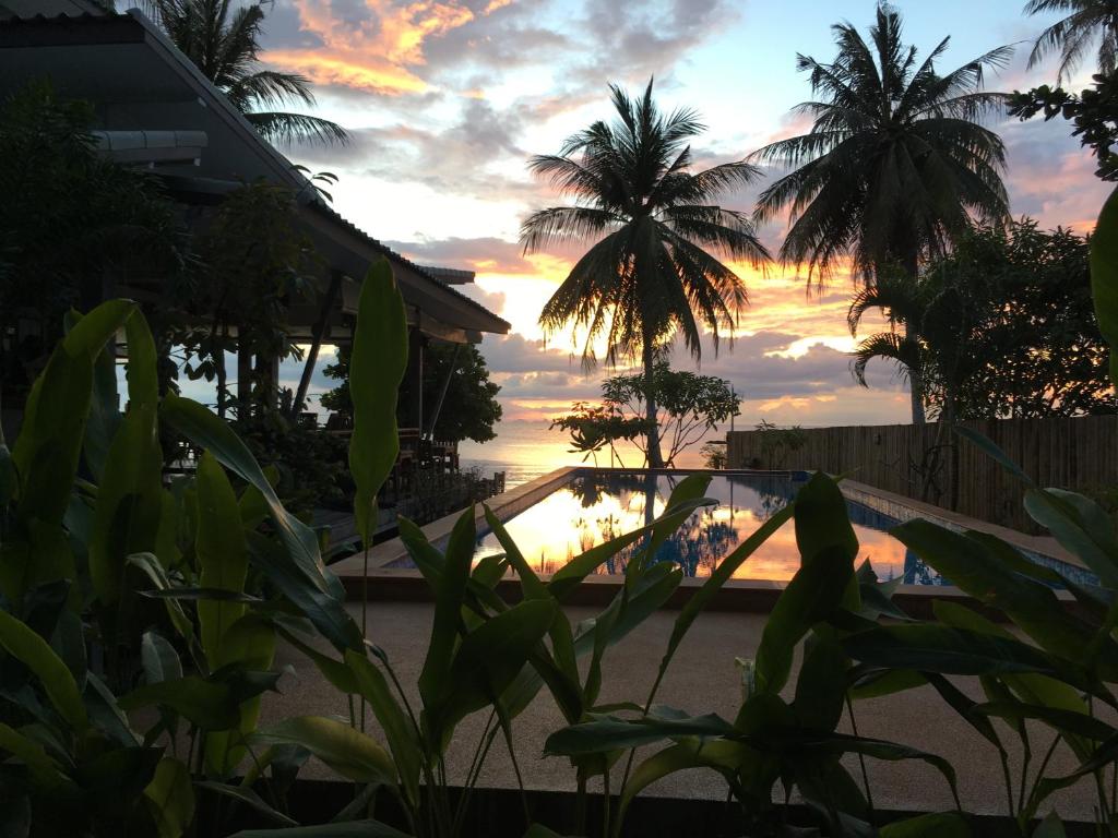 a sunset over a swimming pool with palm trees at Benjamin's Hut in Srithanu
