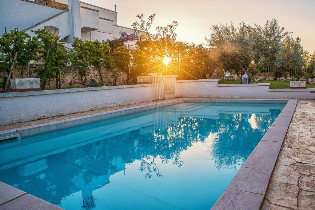 a swimming pool in front of a building with the sun setting at La Casèdde in Cisternino