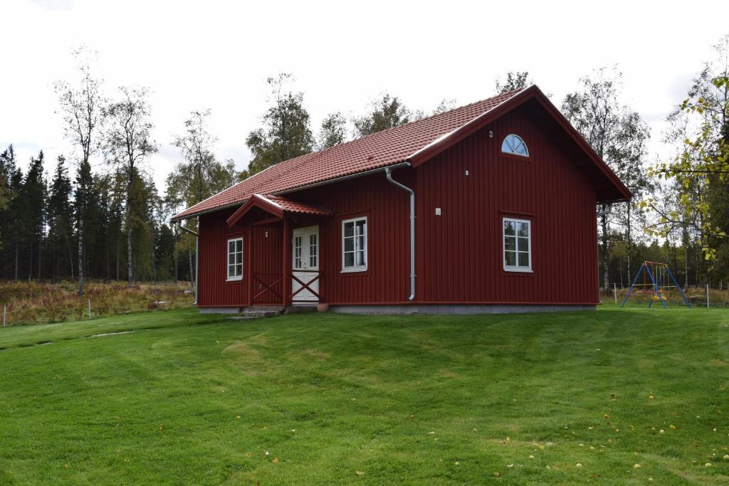 une grange rouge avec une cour herbeuse devant elle dans l'établissement Kronobo, à Marieholm