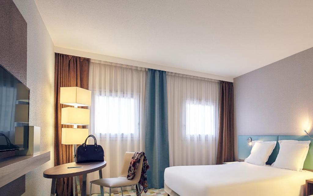 ブシー・サン ・ジョルジュにあるオテル　メルキュール　マルヌ　ラ　ヴァレ　ビュセ　サン　ジョルジュのベッド、デスク、窓が備わるホテルルームです。