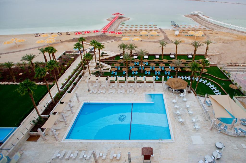 a beach with a pool, chairs, and tables at Herods Dead Sea – A Premium Collection by Fattal Hotels in Neve Zohar
