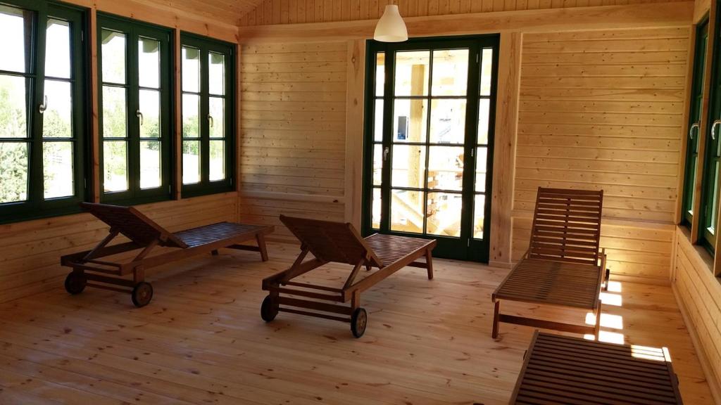 Sunlit wooden relaxation room with three slatted chaise lounges and green-framed windows.