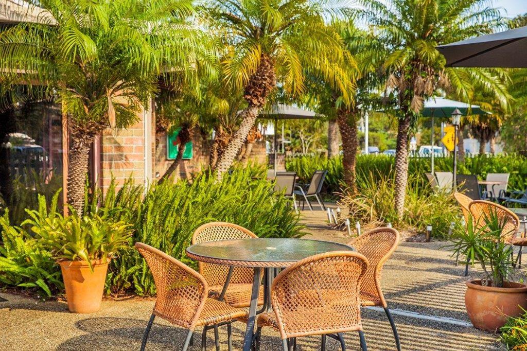 a wooden table with chairs and plants in front of a palm tree at Crescent Head Resort & Conference Centre in Crescent Head