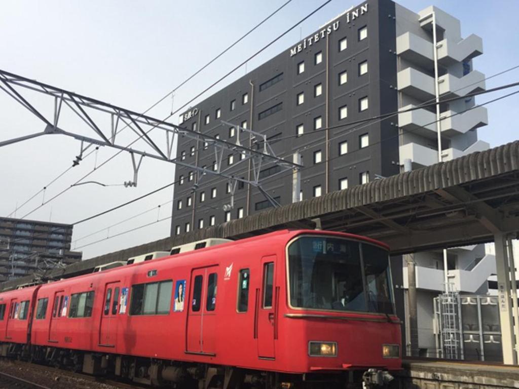 un tren rojo está llegando a una estación de tren en Meitetsu Inn Chita Handa Ekimae, en Handa