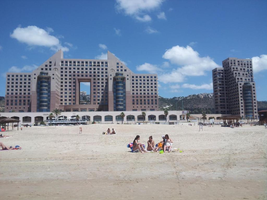 a group of people sitting on a beach with buildings at Haifa Beach Apartment in Haifa
