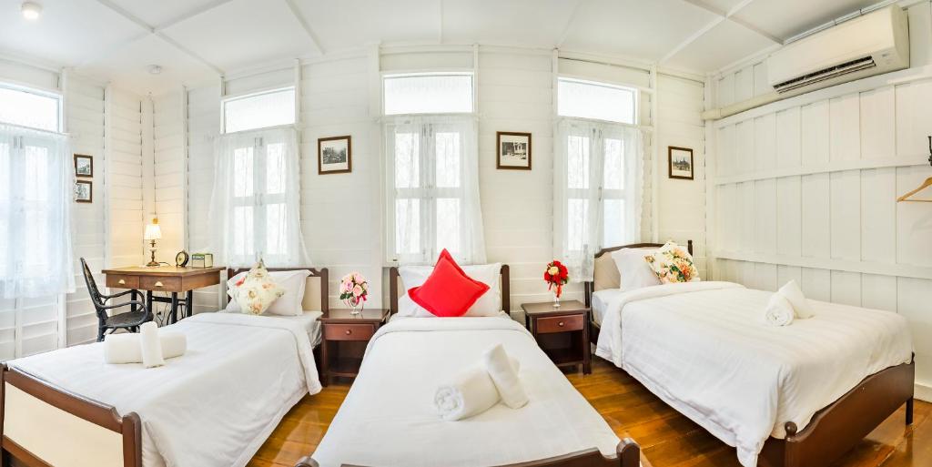 3 camas en una habitación con paredes y ventanas blancas en Baankachitpan Bangkok Hotel en Bangkok