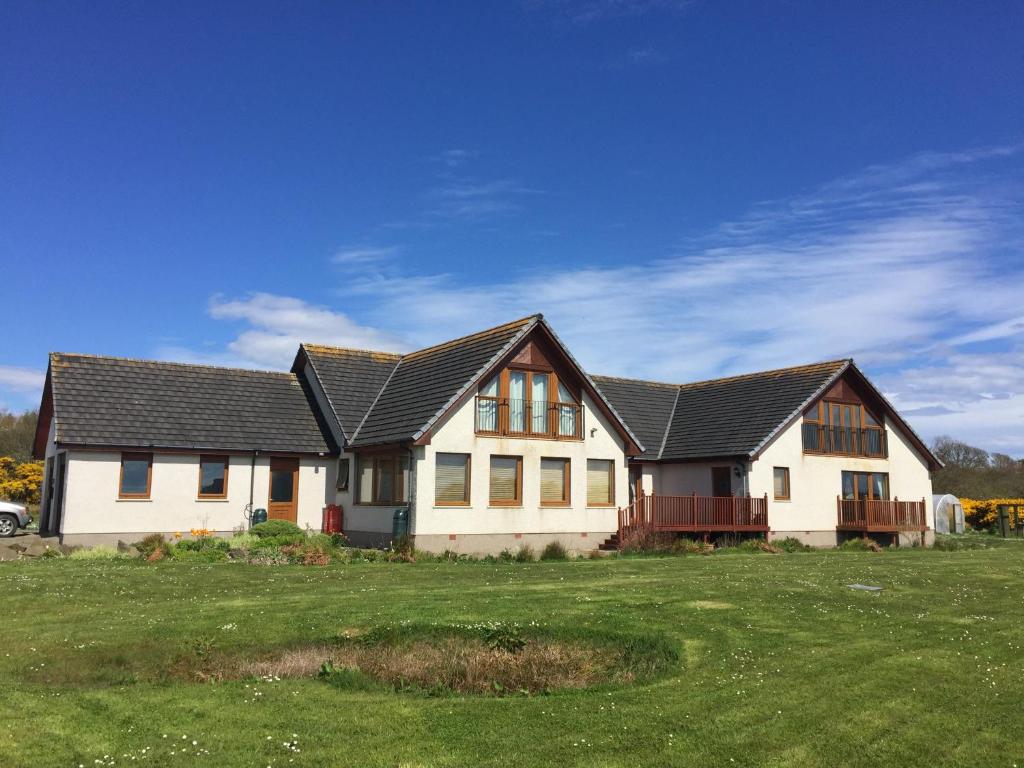 a white house with a black roof on a green field at Acarsaid B&B in Lybster